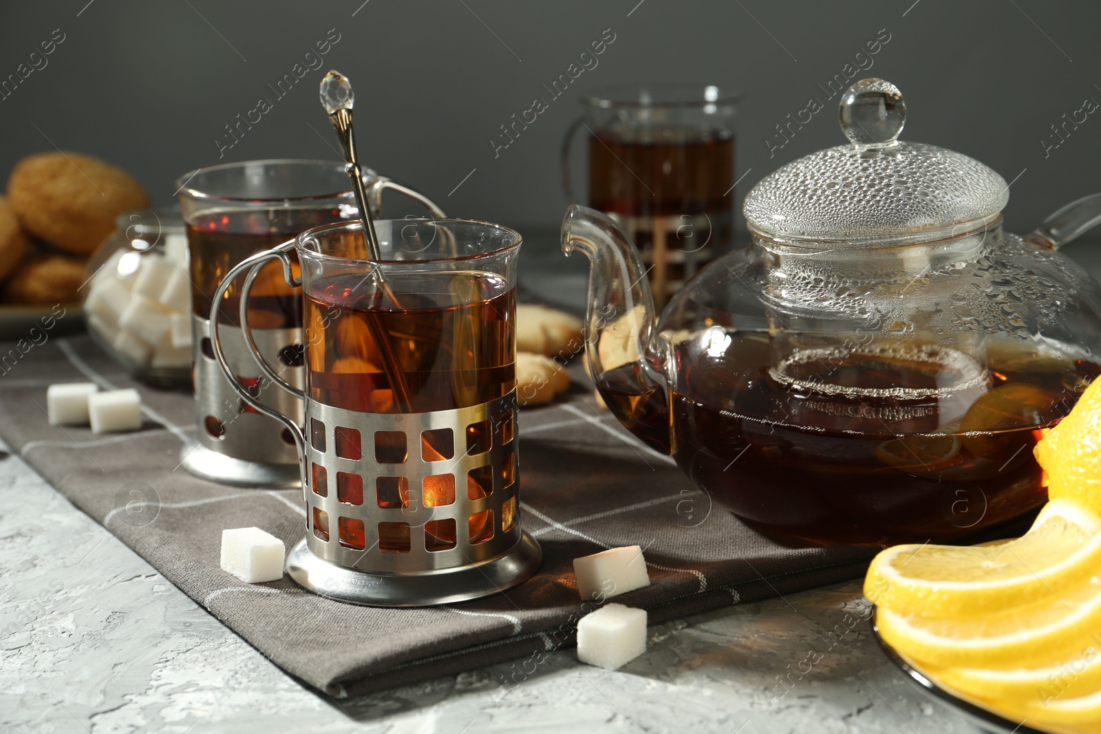 Photo of Glasses of tea in metal holders served on grey textured table