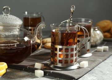 Photo of Glasses of tea in metal holders served on grey textured table, closeup