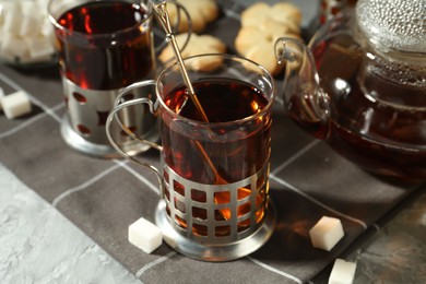 Photo of Glasses of tea in metal holders served on grey textured table, closeup