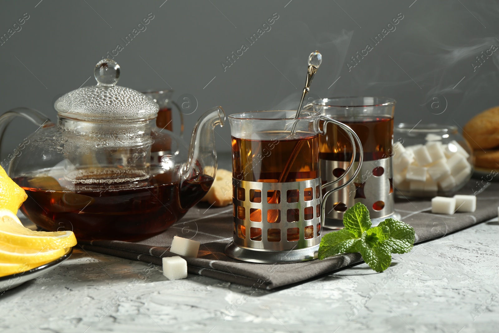 Photo of Glasses of tea in metal holders served on grey textured table