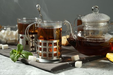 Photo of Glasses of tea in metal holders served on grey textured table, closeup