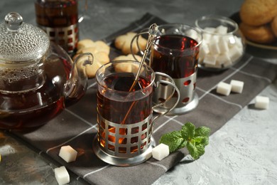 Photo of Glasses of tea in metal holders served on grey textured table, closeup