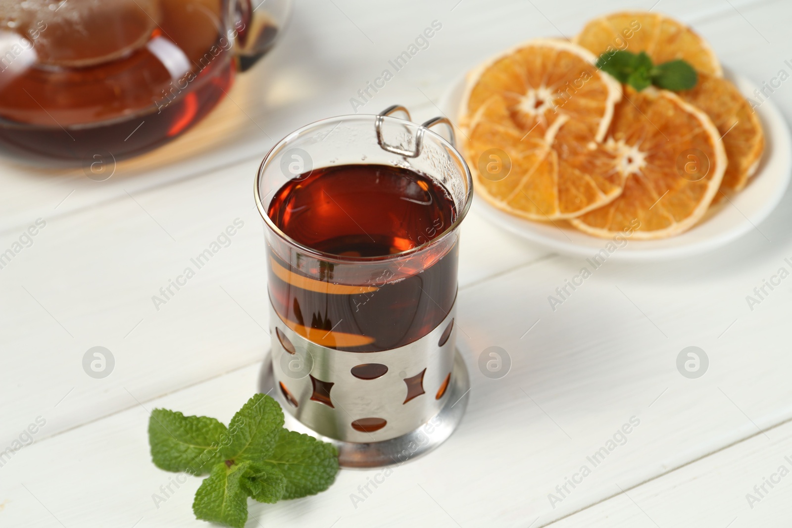 Photo of Glass of tea in metal holder served on white wooden table, closeup