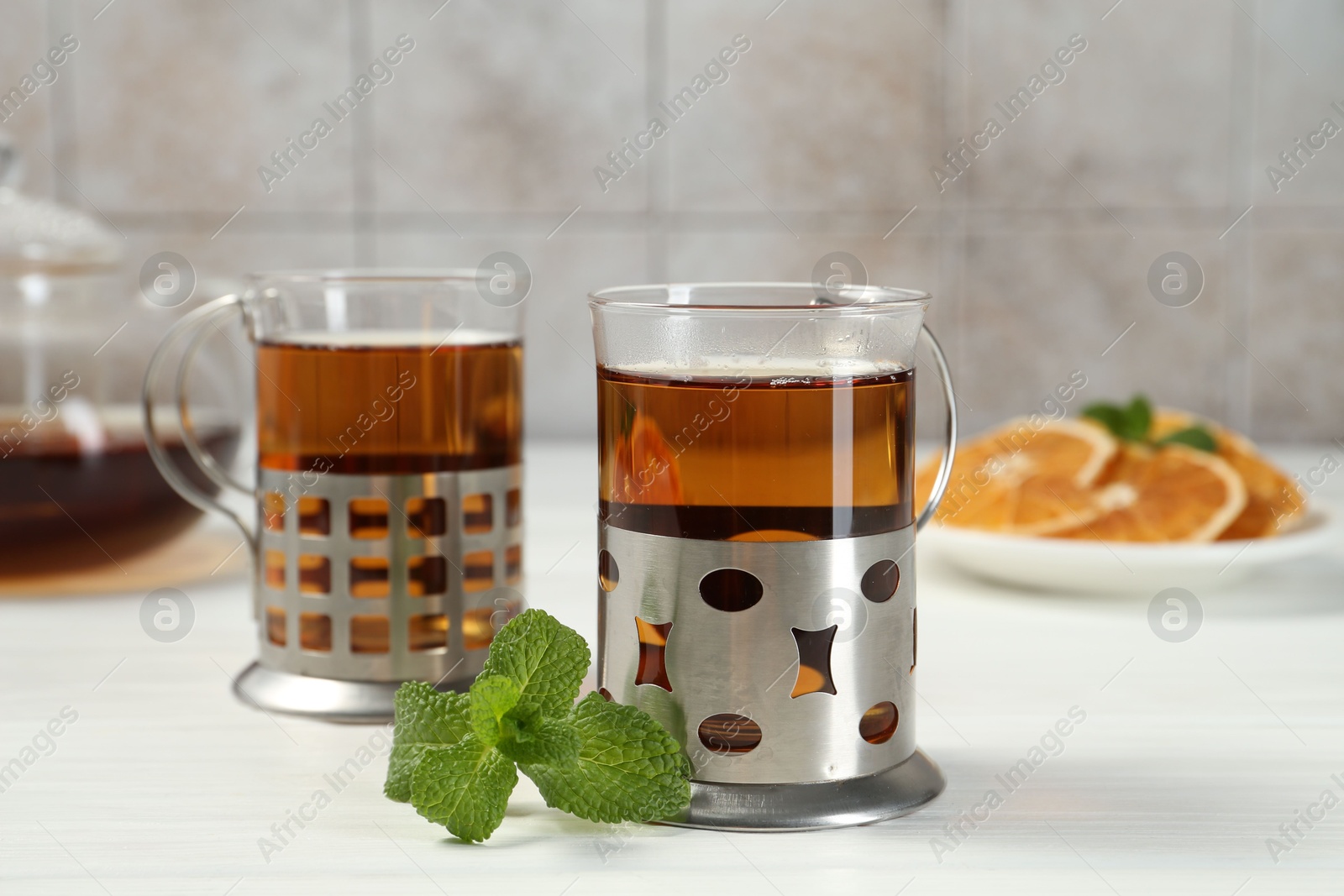 Photo of Glasses of tea in metal holders served on white wooden table, closeup