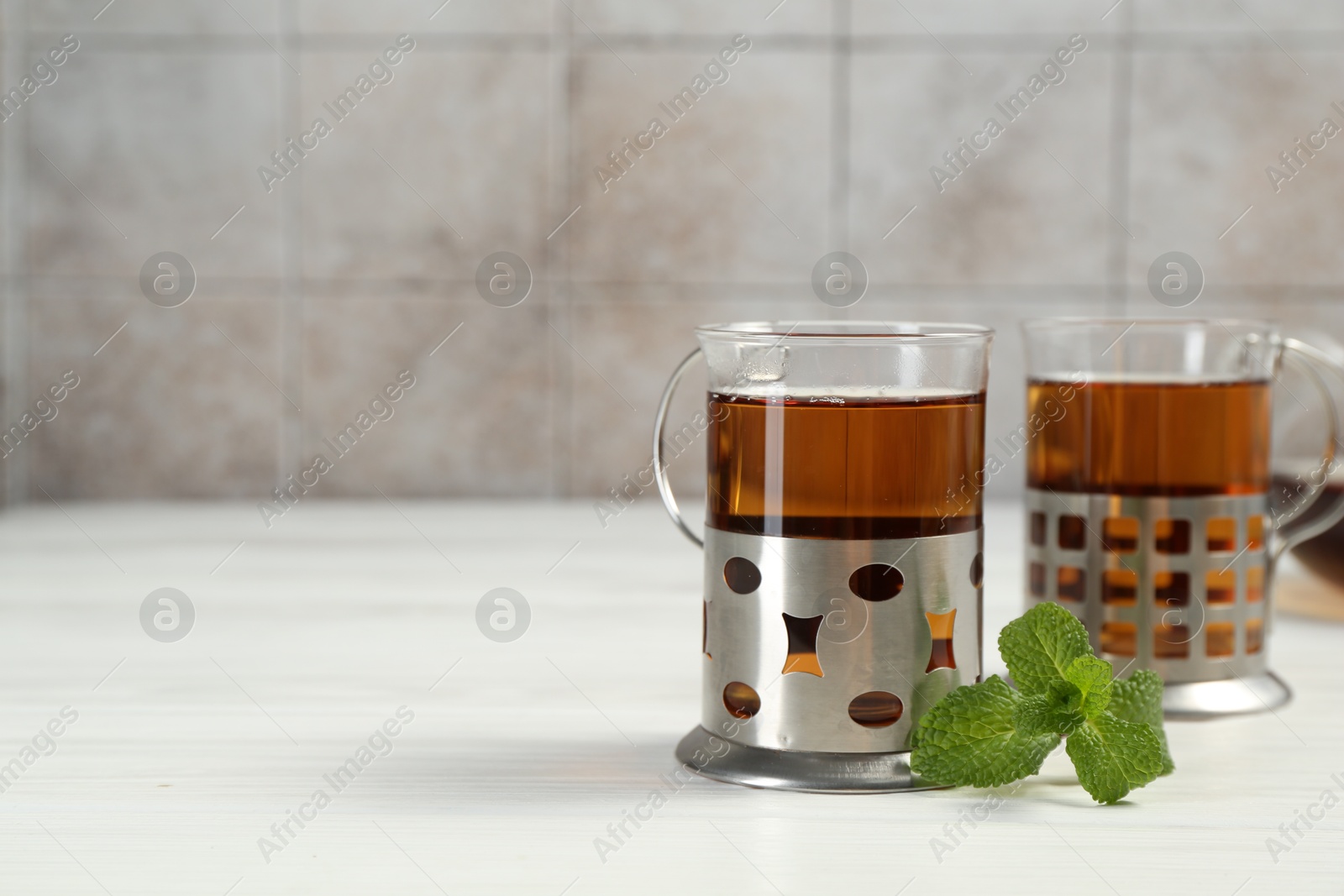 Photo of Glasses of tea in metal holders served on white wooden table, closeup. Space for text