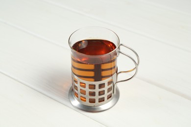 Glass cup of tea in metal holder on white wooden table, closeup