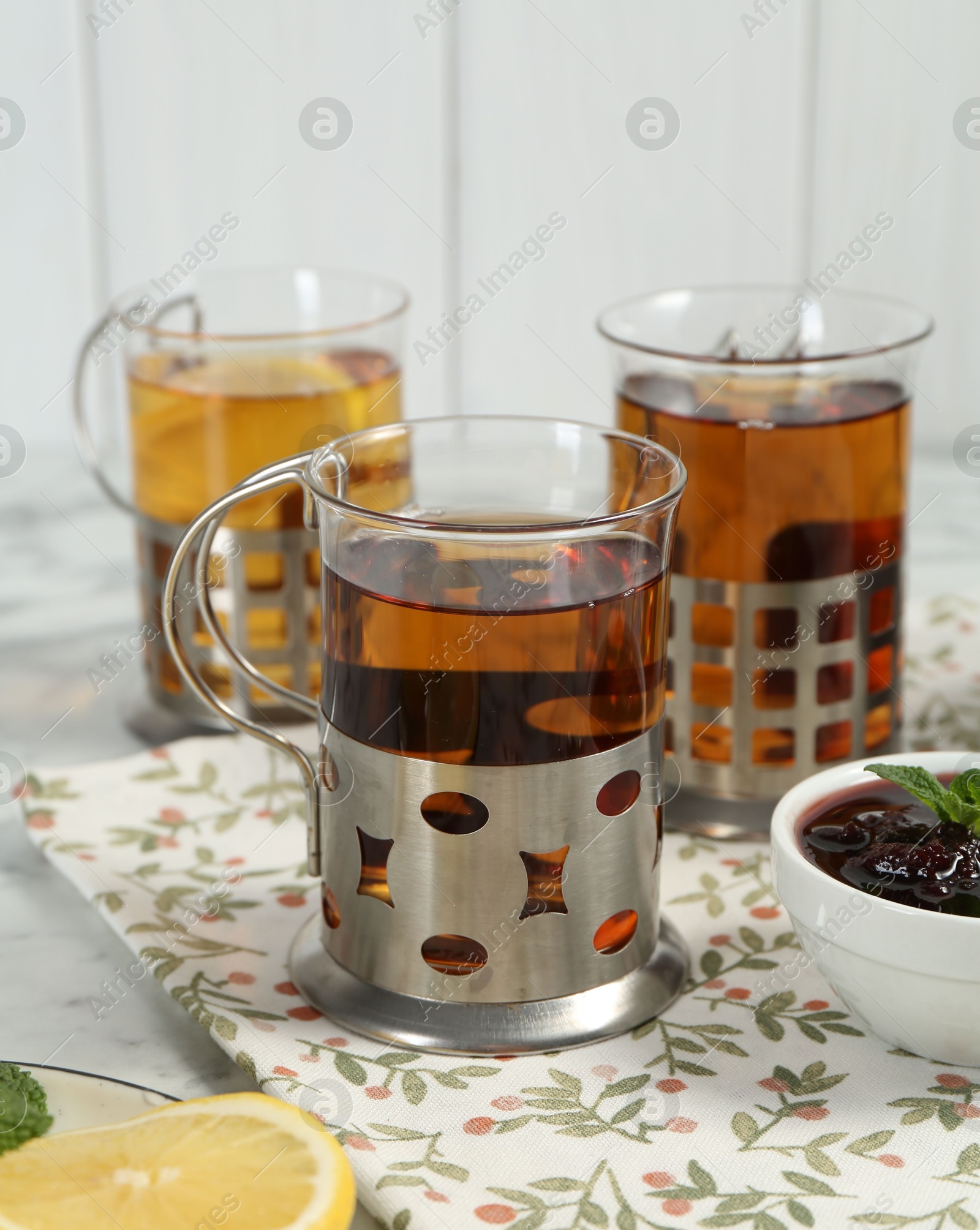 Photo of Glasses of tea in metal holders served on white table, closeup