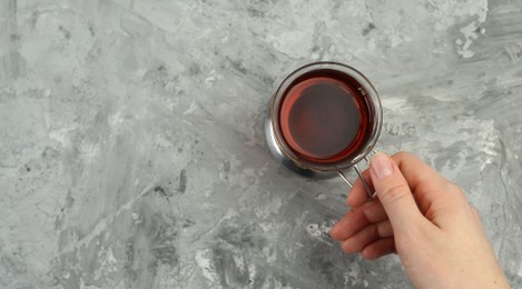 Woman with glass of tea in metal holder at grey textured table, top view. Space for text