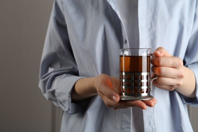 Woman with glass of tea in metal holder on grey background, closeup