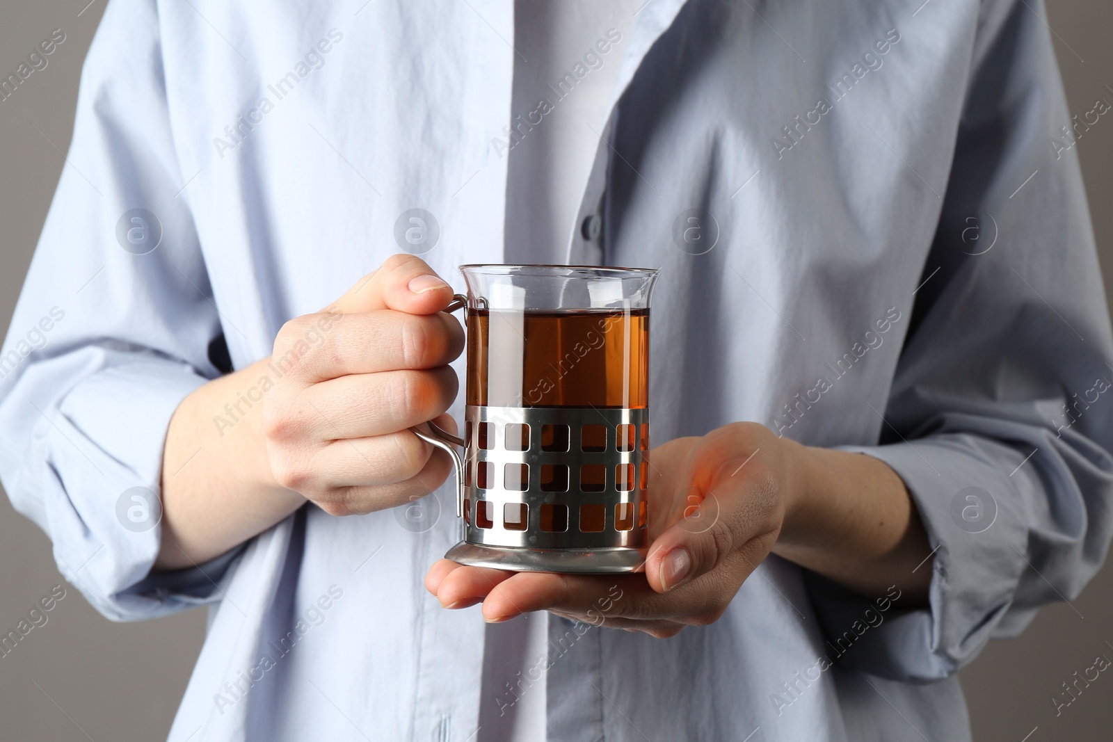 Photo of Woman with glass of tea in metal holder on grey background, closeup