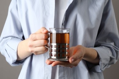 Woman with glass of tea in metal holder on grey background, closeup