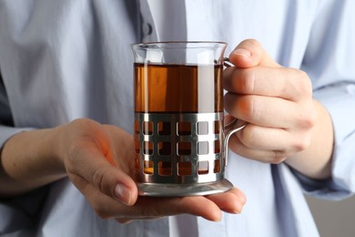 Photo of Woman with glass of tea in metal holder on grey background, closeup