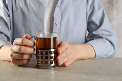 Woman with glass of tea in metal holder at beige table, closeup