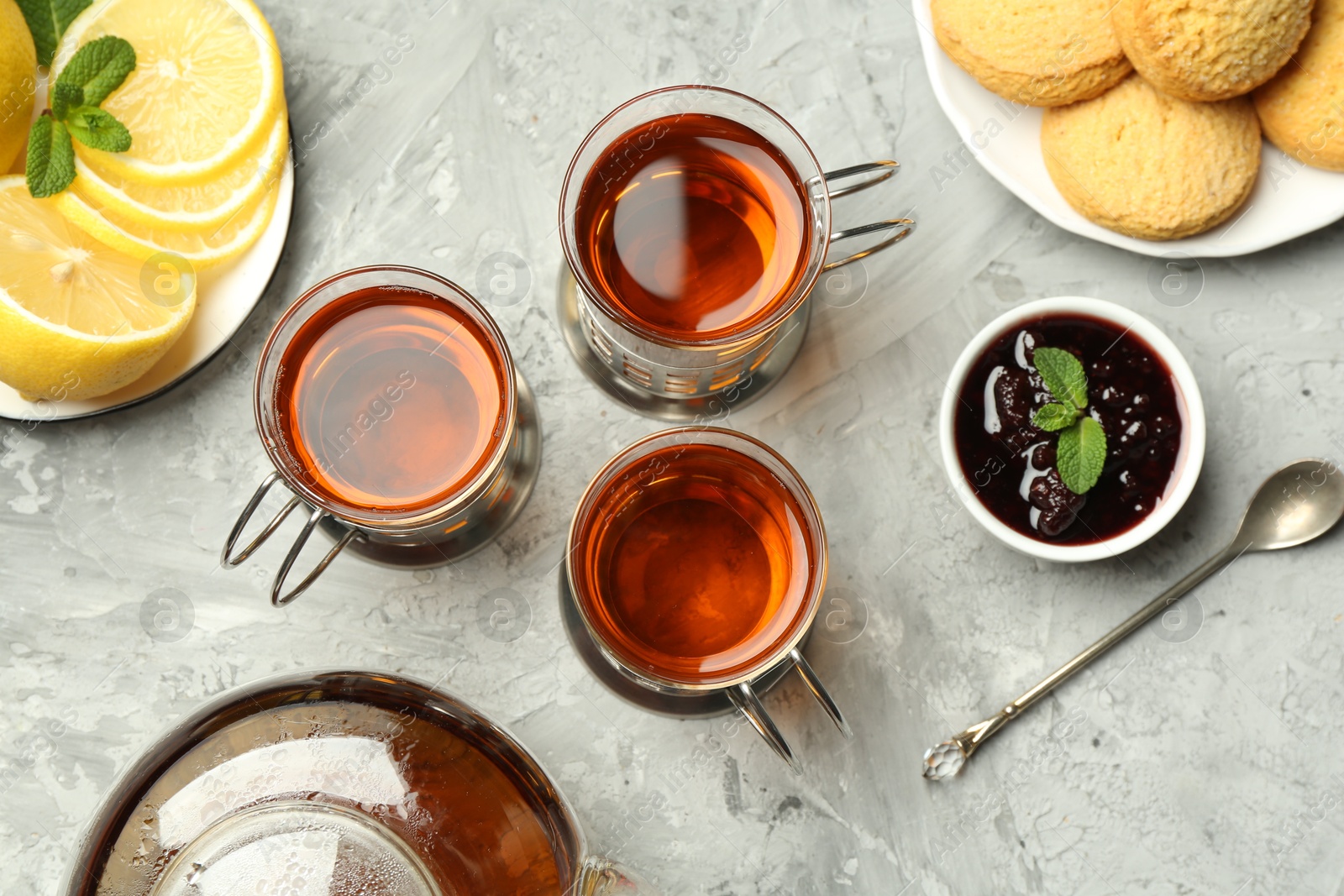 Photo of Glasses of tea in metal holders served on grey textured table, flat lay