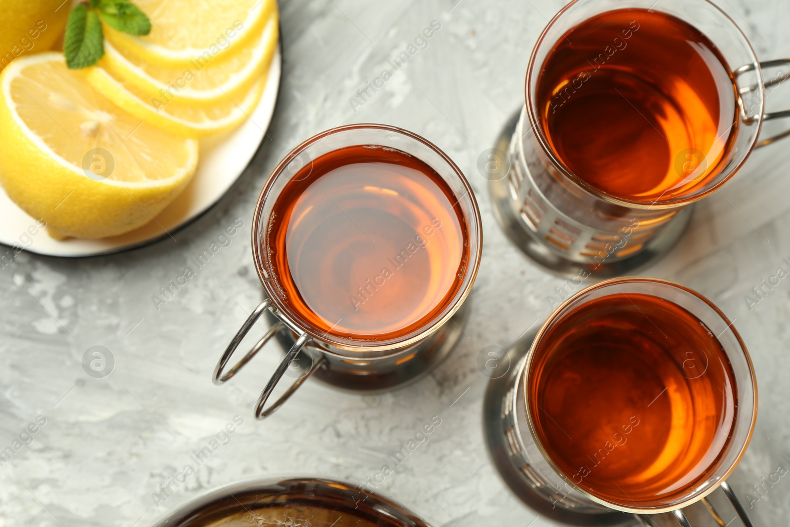 Photo of Glasses of tea in metal holders served on grey textured table, flat lay