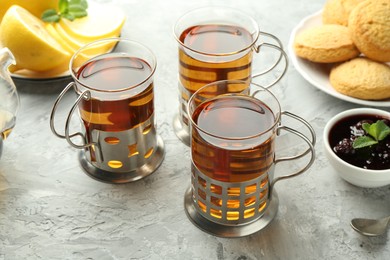 Photo of Glasses of tea in metal holders served on grey textured table, closeup