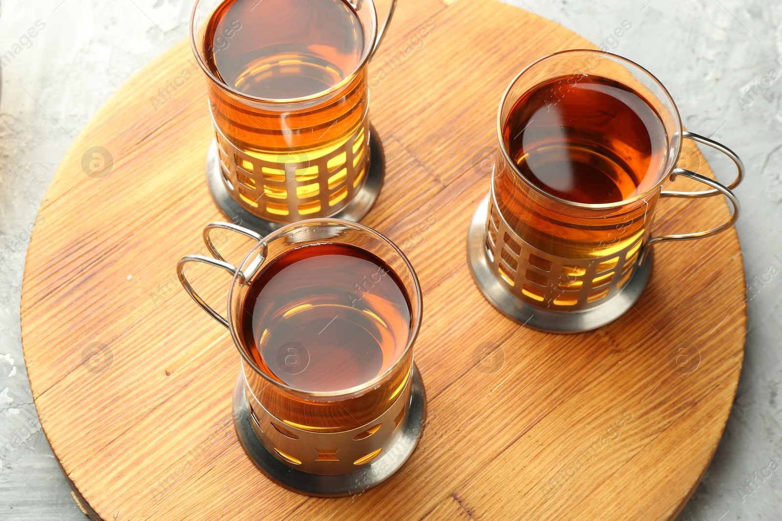 Photo of Glasses of tea in metal holders served on grey textured table, closeup