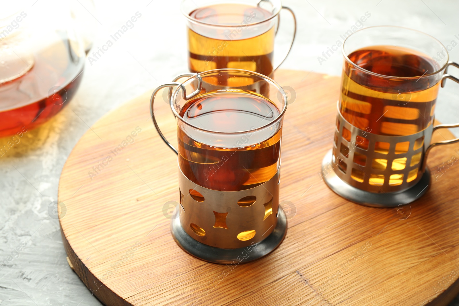 Photo of Glasses of tea in metal holders served on grey textured table, closeup