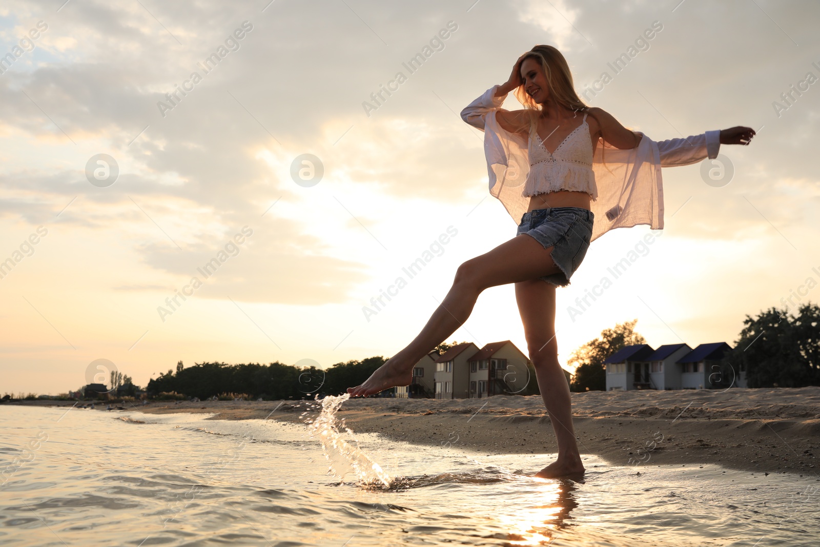 Photo of Beautiful young woman playing near water on sea beach, space for text