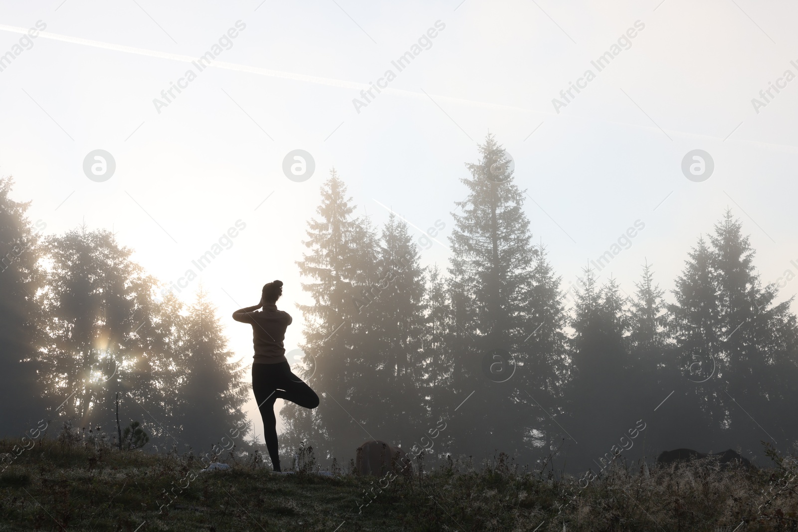 Photo of Woman practicing yoga in mountains at sunrise, back view