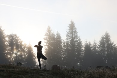 Photo of Woman practicing yoga in mountains at sunrise, back view