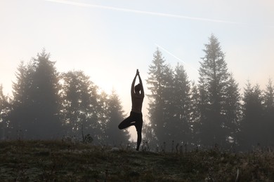 Photo of Woman practicing yoga in mountains at sunrise, back view