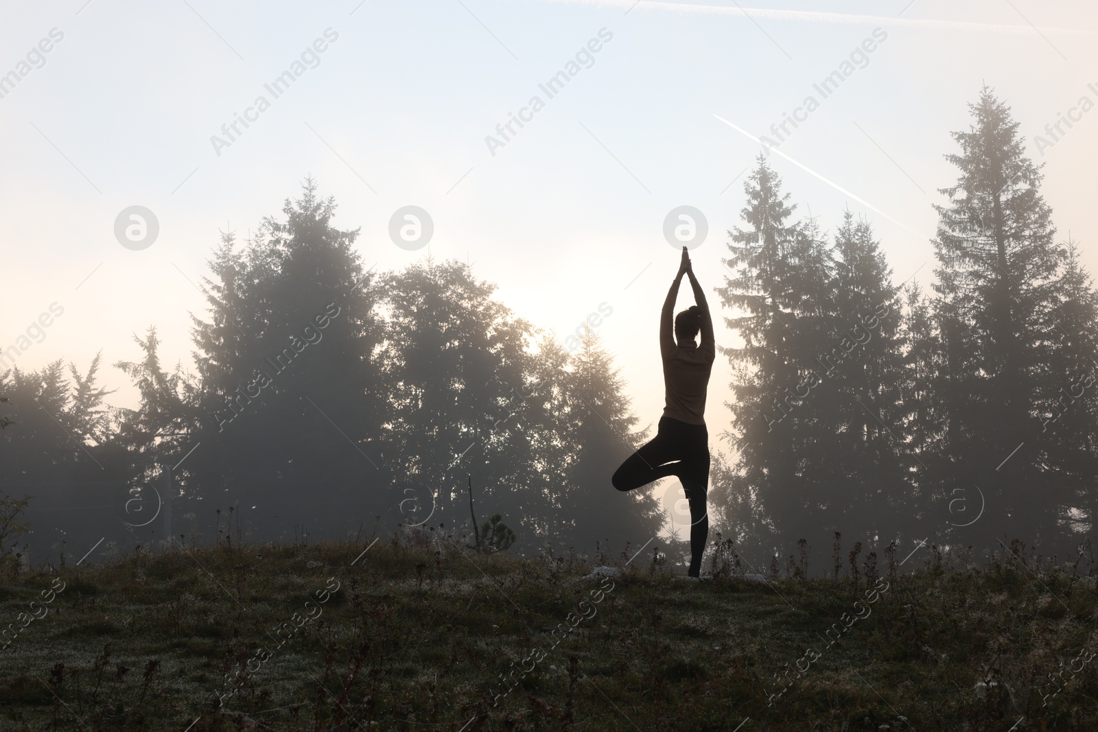 Photo of Woman practicing yoga in mountains at sunrise, back view