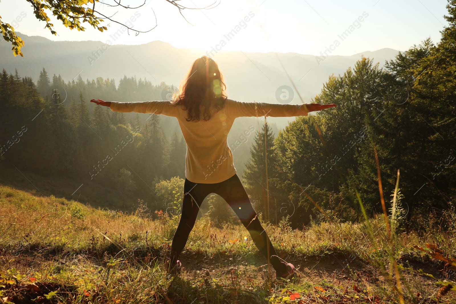 Photo of Woman practicing yoga in mountains at sunrise, back view