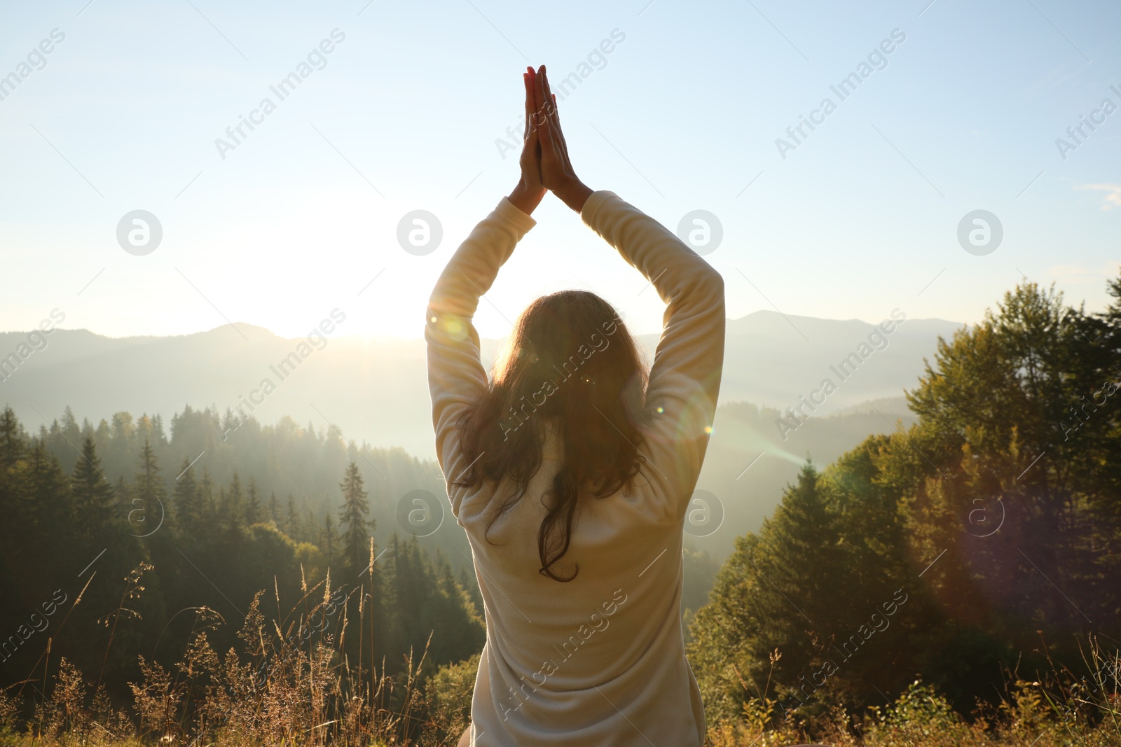 Photo of Woman practicing yoga in mountains at sunrise, back view