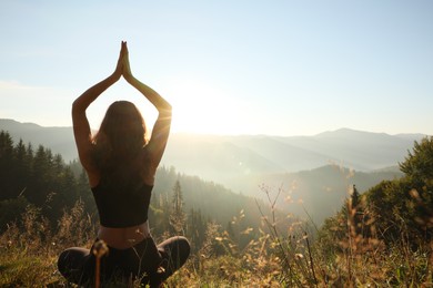 Photo of Woman practicing yoga in mountains at sunrise, back view