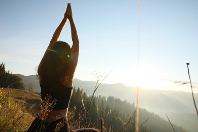 Photo of Woman practicing yoga in mountains at sunrise, back view