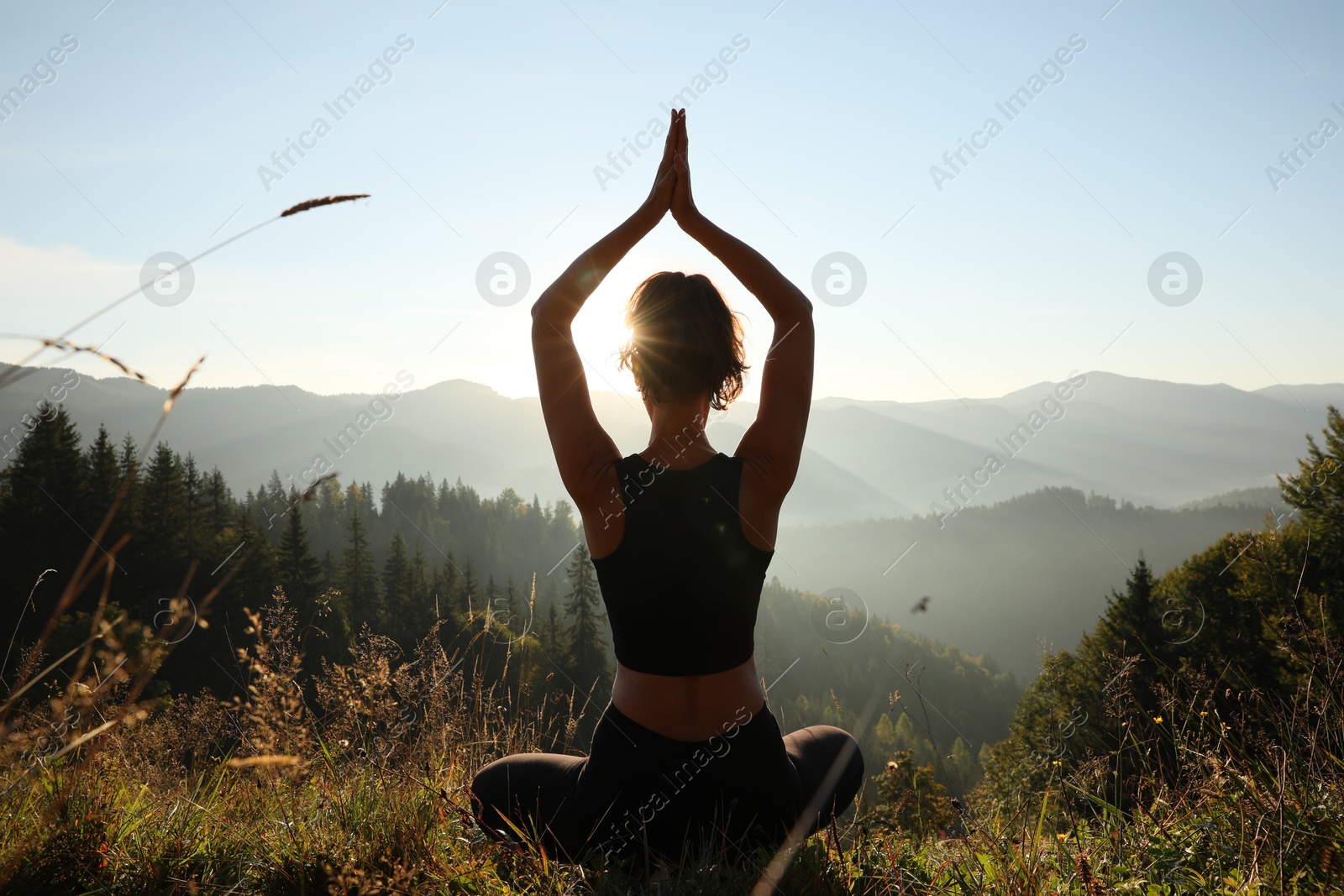 Photo of Woman practicing yoga in mountains at sunrise, back view