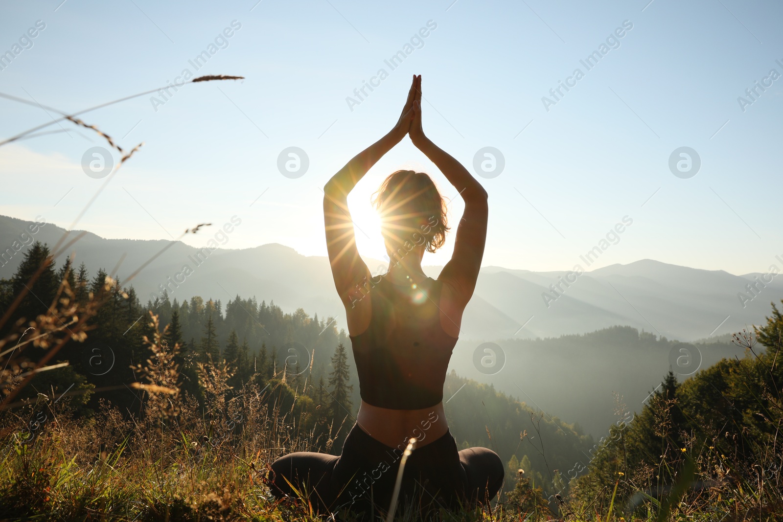 Photo of Woman practicing yoga in mountains at sunrise, back view