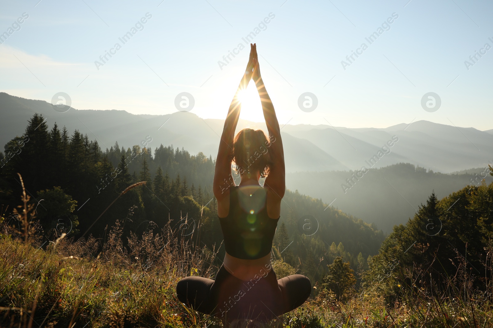 Photo of Woman practicing yoga in mountains at sunrise, back view