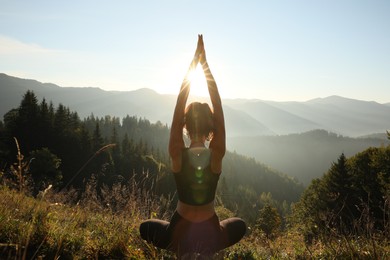 Woman practicing yoga in mountains at sunrise, back view