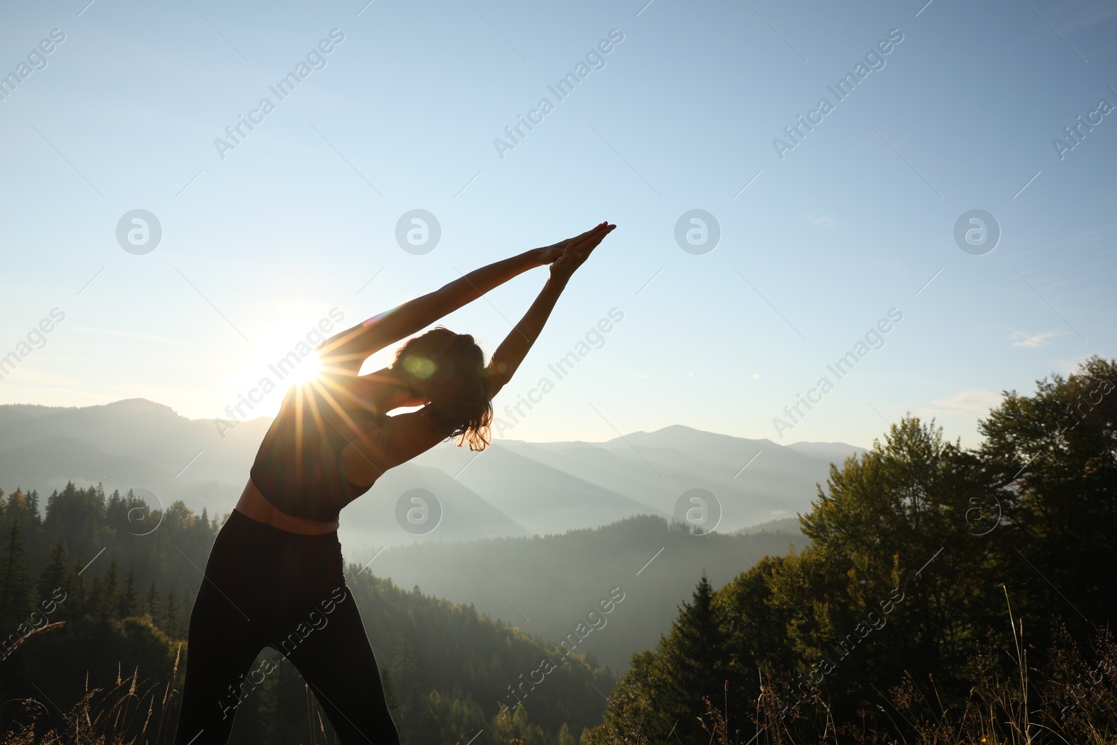 Photo of Woman practicing yoga in mountains at sunrise, back view