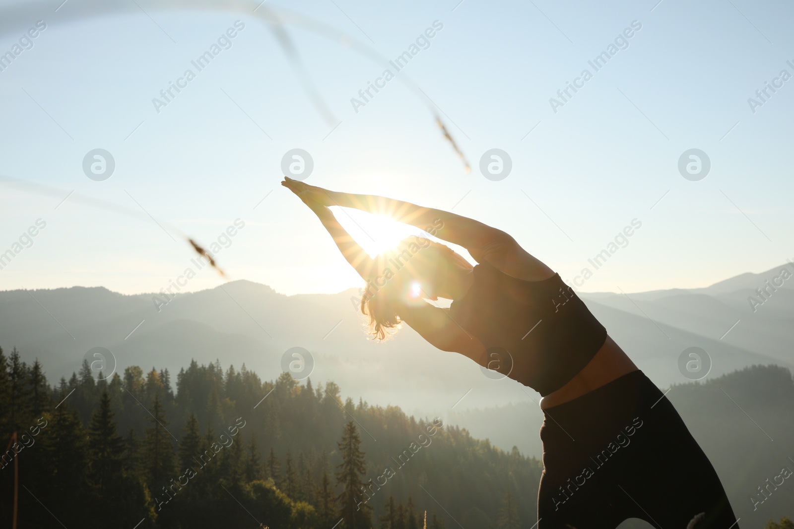 Photo of Woman practicing yoga in mountains at sunrise, back view