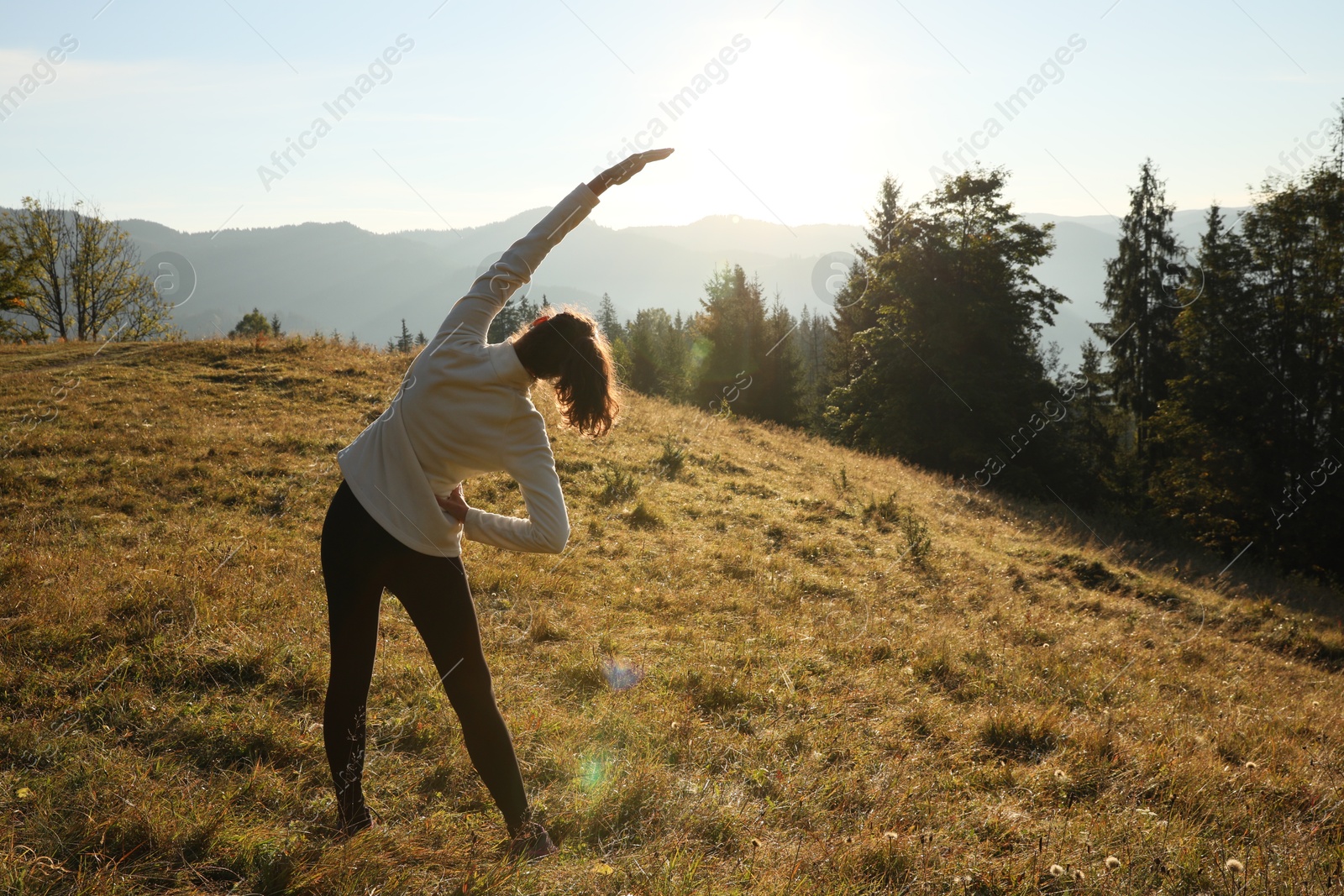 Photo of Woman practicing yoga in mountains at sunrise, back view