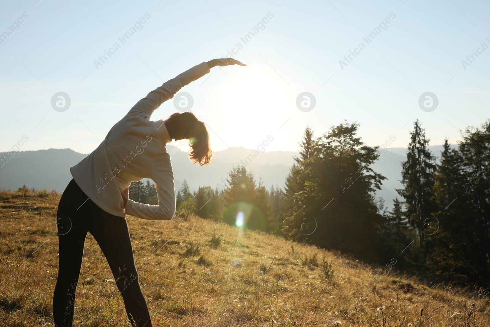 Photo of Woman practicing yoga in mountains at sunrise, back view