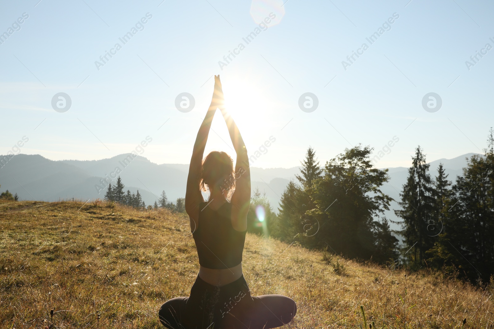 Photo of Woman practicing yoga in mountains at sunrise, back view