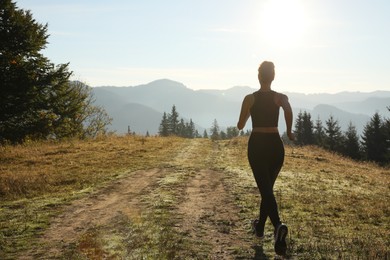 Photo of Sporty woman running in mountains, back view