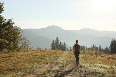 Photo of Sporty woman running in mountains, back view