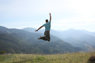 Photo of Sporty man jumping on grassy hill in mountains