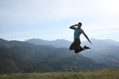 Sporty man jumping on grassy hill in mountains