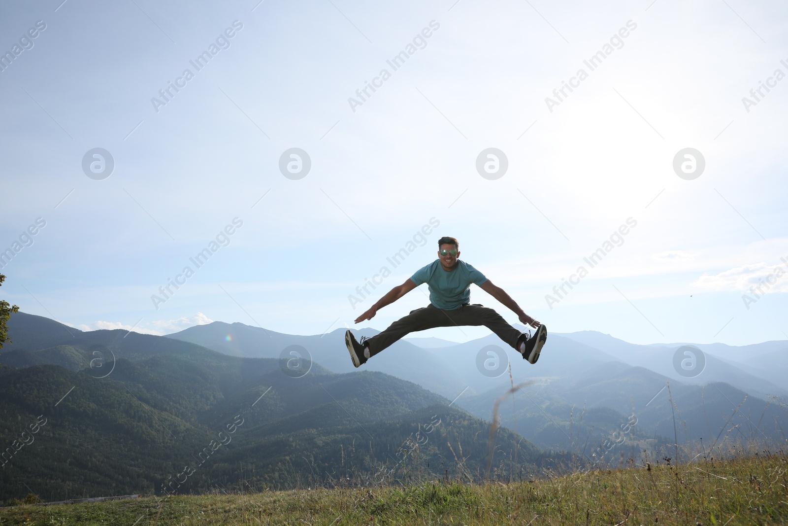 Photo of Sporty man jumping on grassy hill in mountains