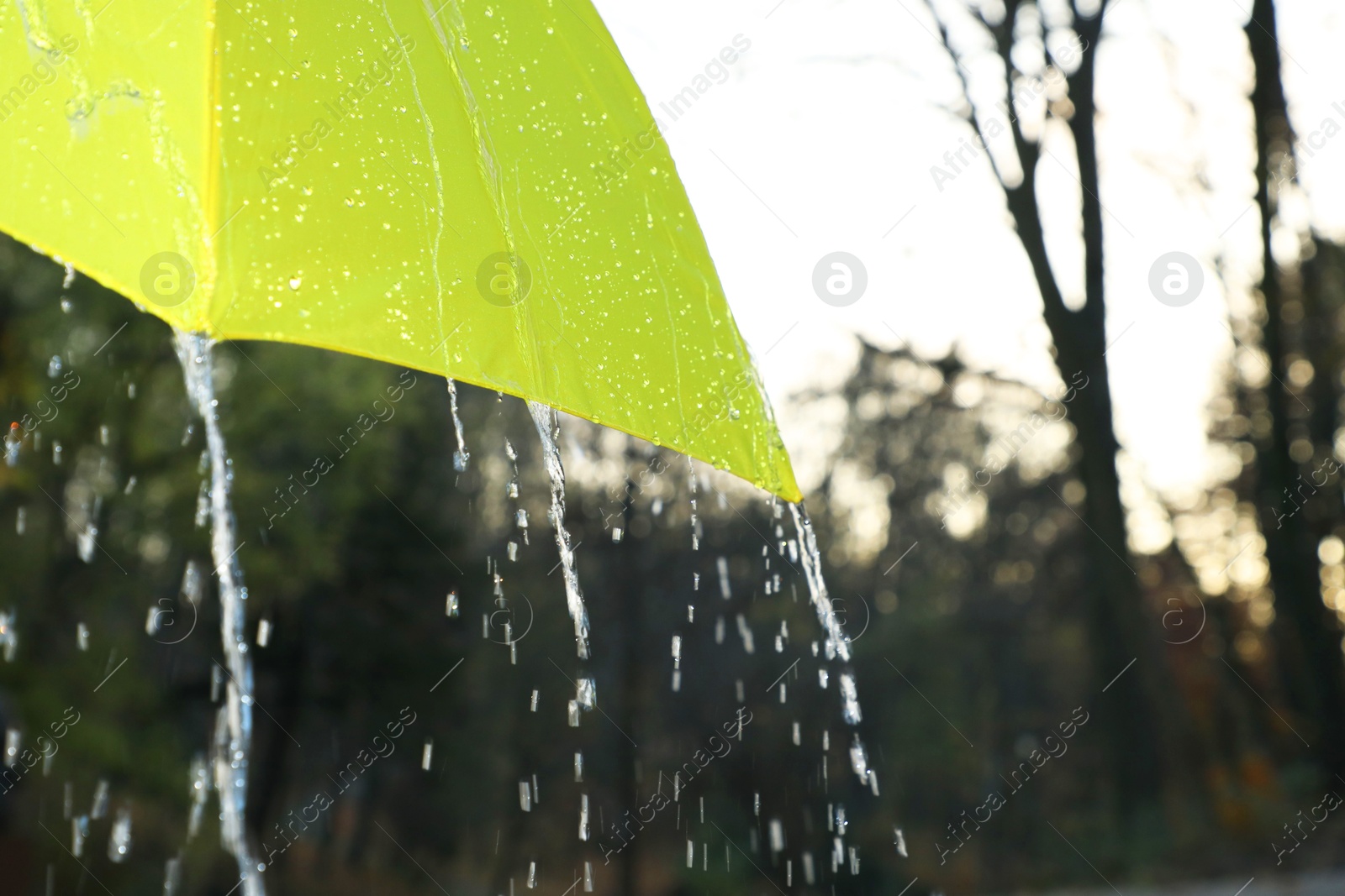 Photo of Open yellow umbrella under pouring rain outdoors, closeup