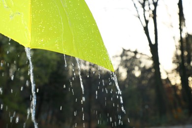 Photo of Open yellow umbrella under pouring rain outdoors, closeup