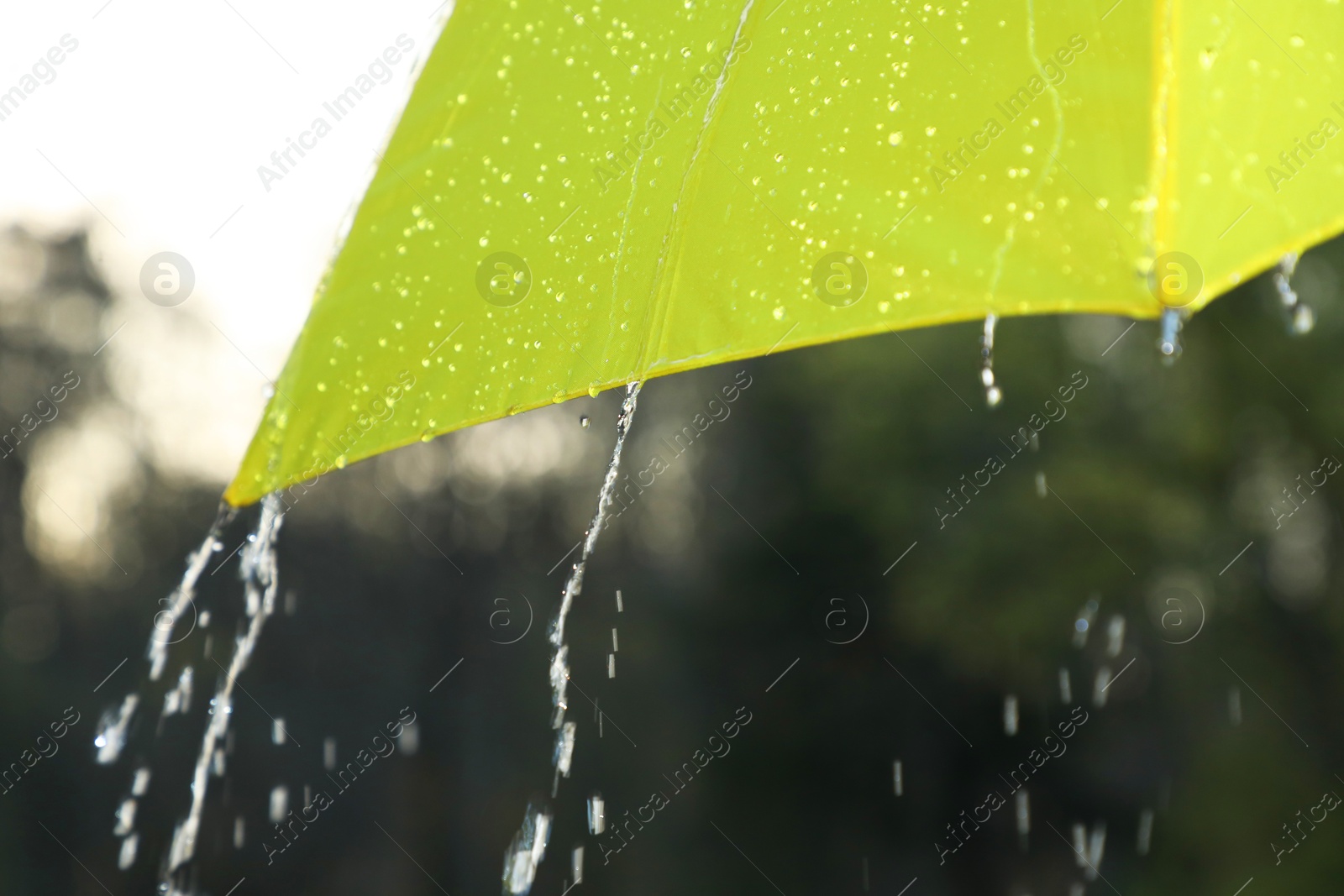 Photo of Open yellow umbrella under pouring rain outdoors, closeup