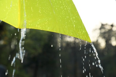 Photo of Open yellow umbrella under pouring rain outdoors, closeup