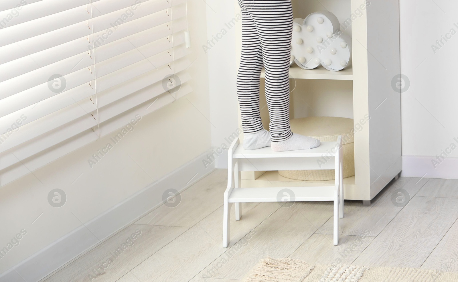 Photo of Little girl standing on step stool indoors, closeup. Space for text